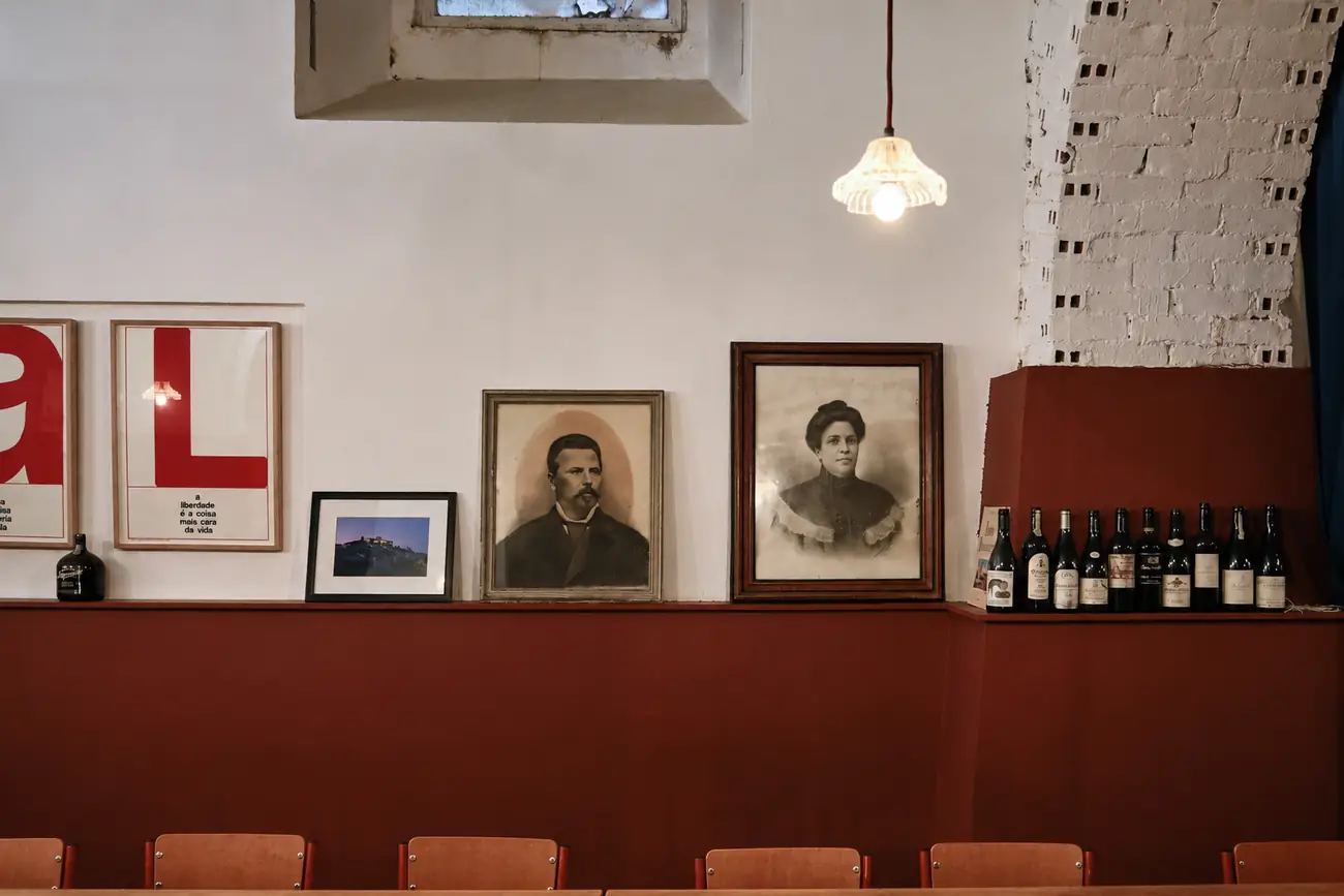 Balcão com garrafas e cartazes tipográficos vermelhos ao fundo da sala.