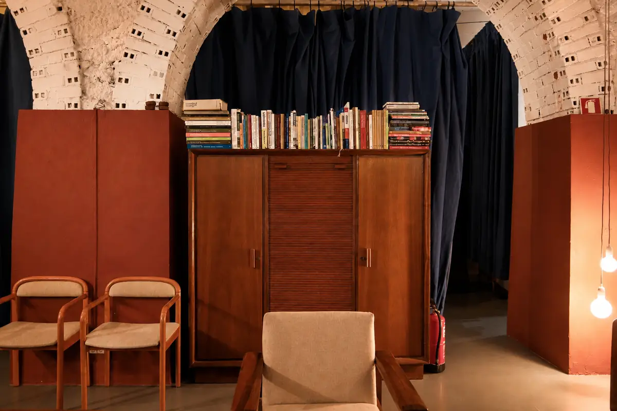 Armário de madeira com livros empilhados e cortina azul atrás.