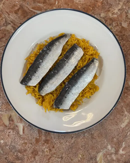 Prato de sardinhas sobre arroz de açafrão, visto de cima.