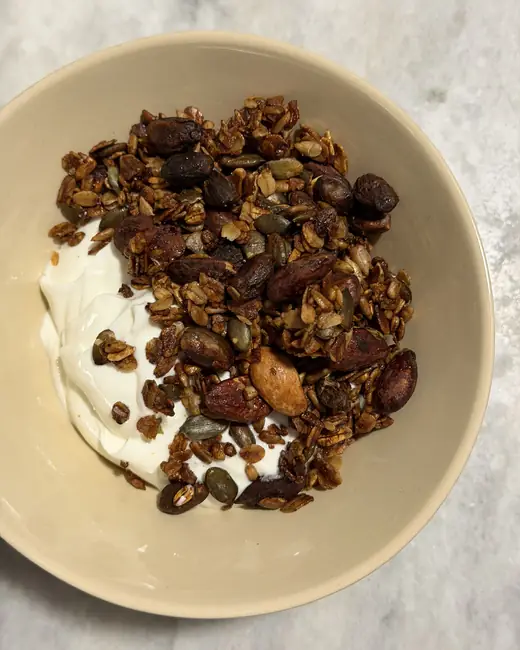 Tigela de iogurte com granola de frutos secos e sementes, servida ao pequeno-almoço.