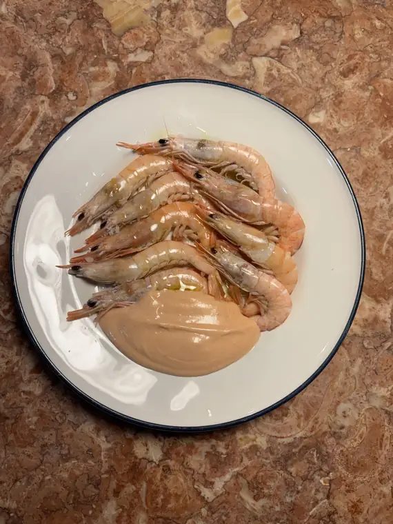 Prato de camarão cozido com um creme claro ao lado.