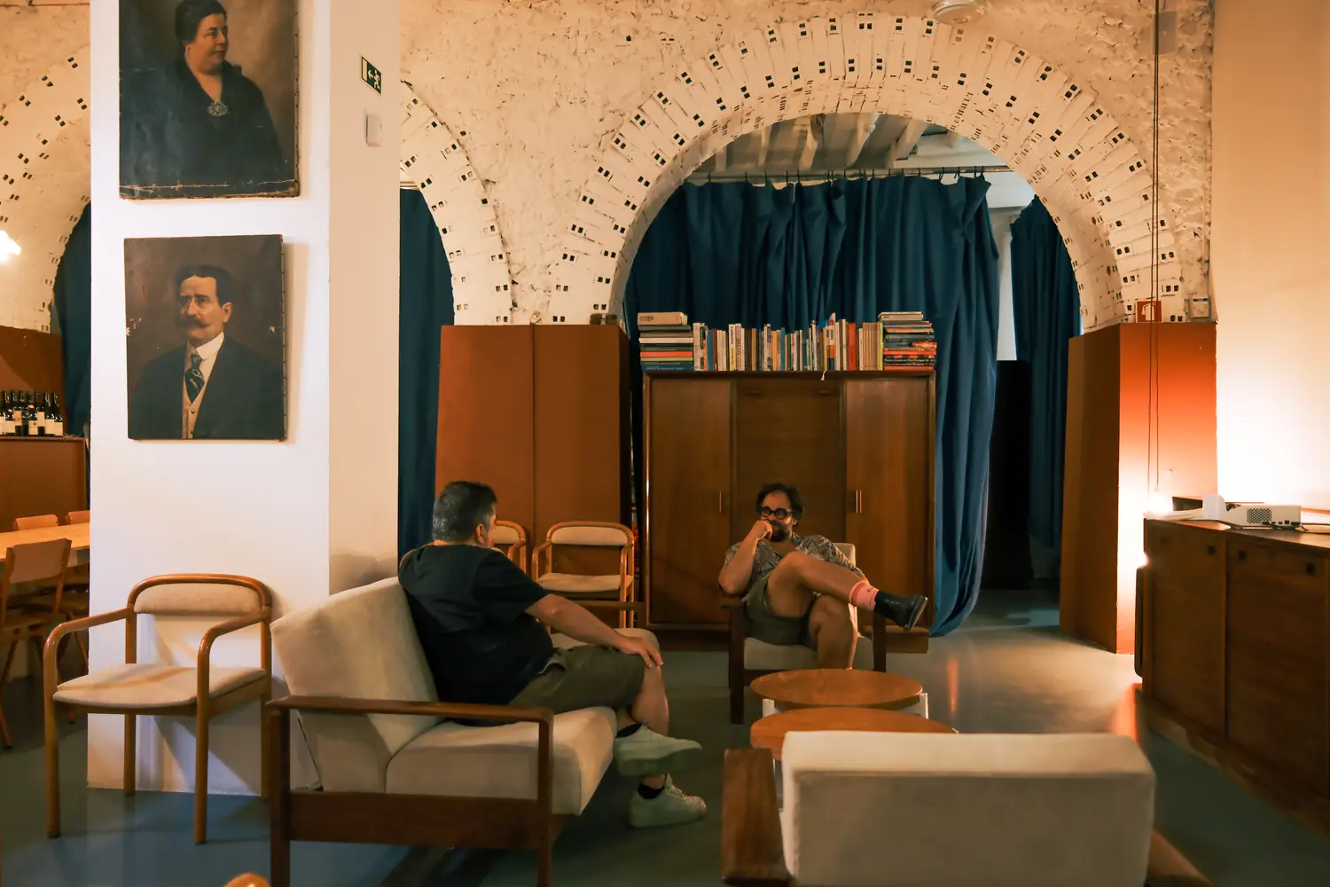 Zona de estar com sofá, cadeirões e retratos a óleo nas paredes.