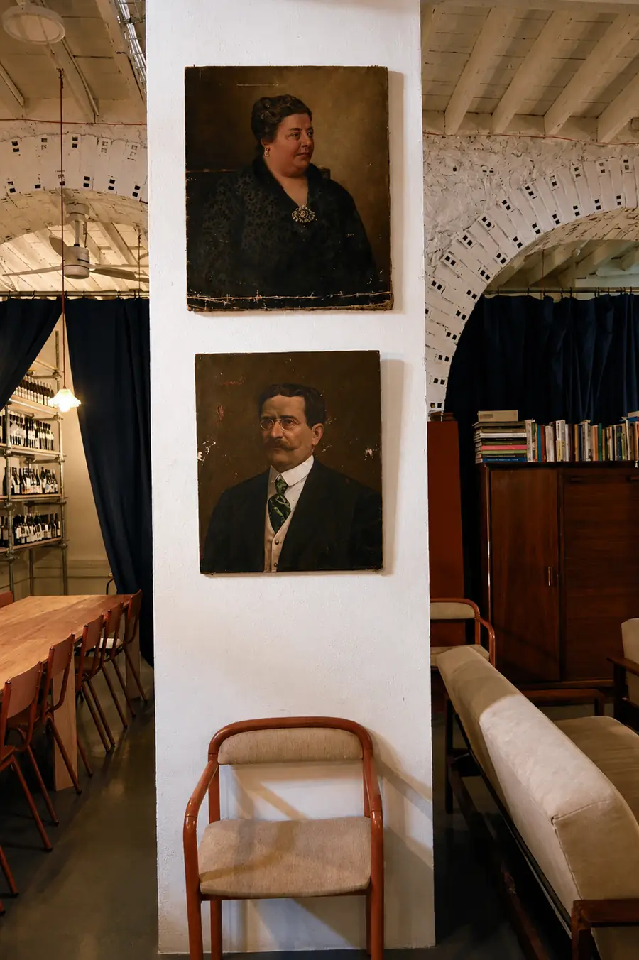 Dois retratos a óleo pendurados numa parede branca de tijolo.